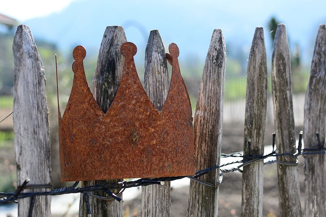 Eine verrostete Krone aus Metall aufgehängt an einem Zaun aus Holz.
