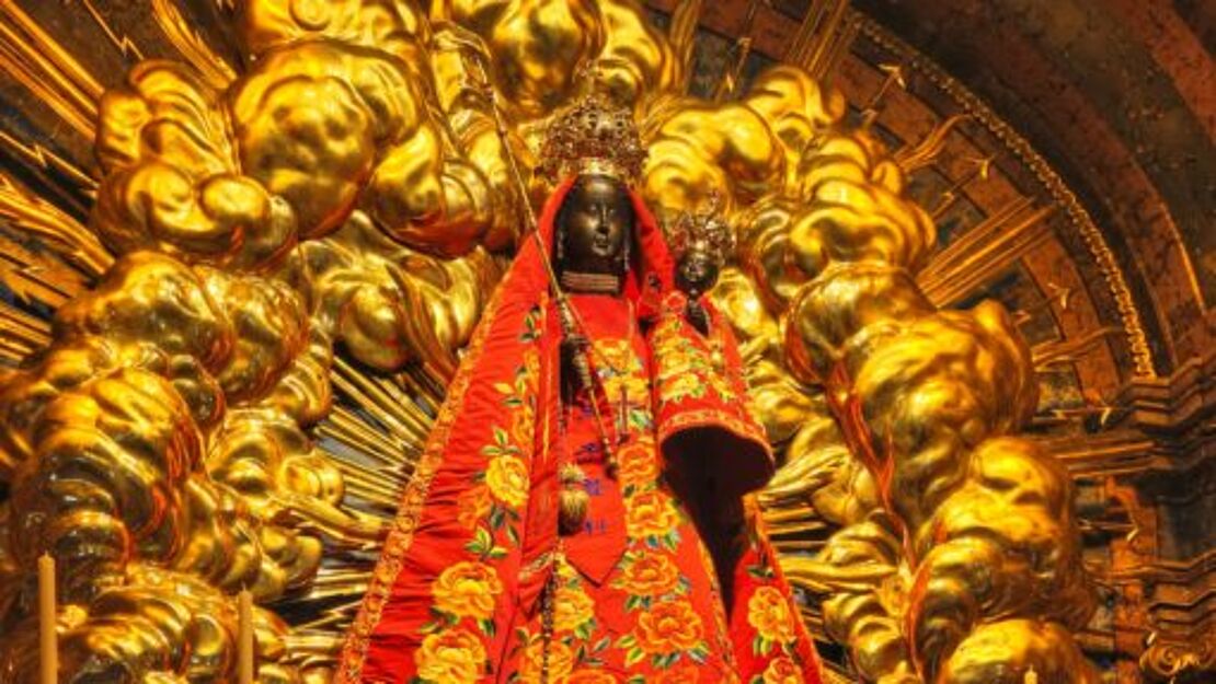Eine göttliche Statue eine Frau mit einem Kind auf dem Arm vor einer goldenen Wand.