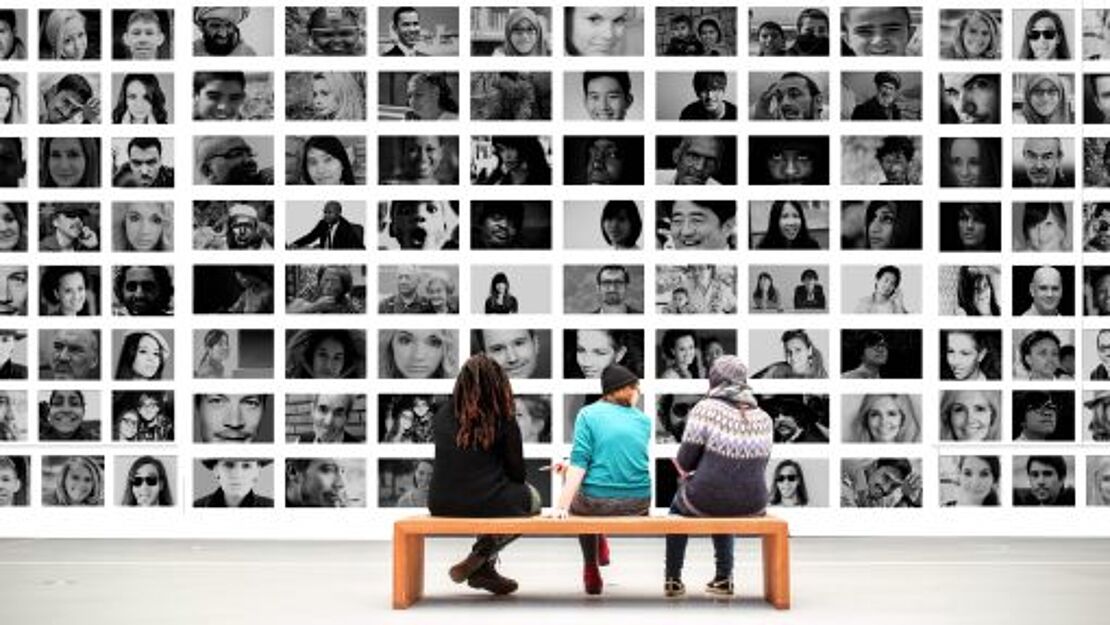 Drei kunstinteressierte Personen sitzen auf einer Bank in einem Museum vor einer Wand voller Menschen-Portraits.
